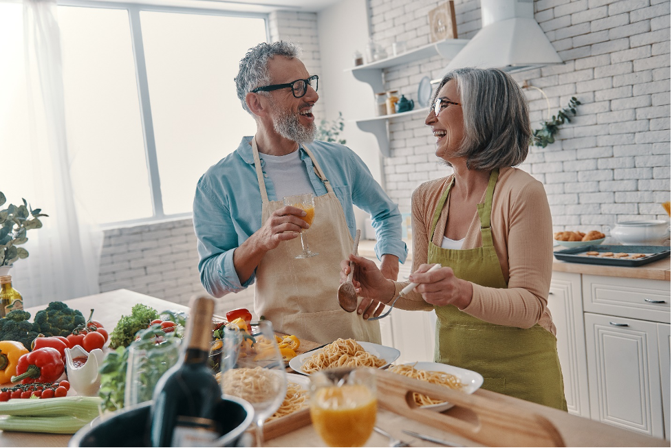 Senior couple make dinner together while laughing in the kitchen.