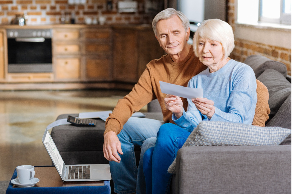 Elderly couple looks over check as they go through finances on the sofa.