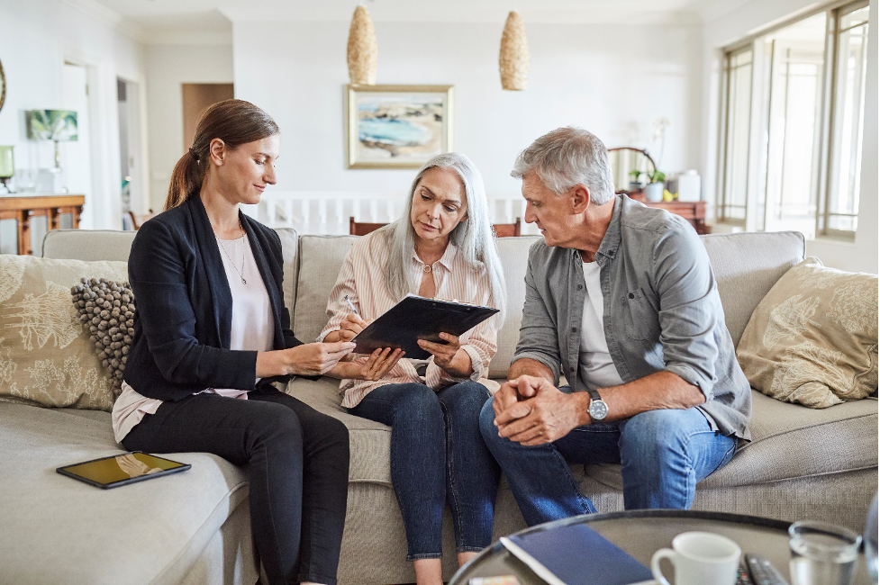 Mature woman signing contract while sitting with insurance agent. Female financial advisor is with couple at home. They are in living room by Morsa Images/istockphoto
